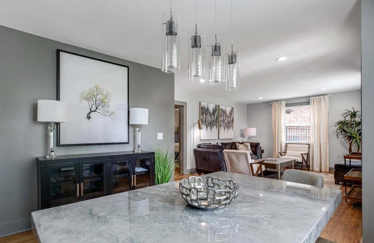 A stylish dining area featuring a marble dining table, decorative pendant lights, framed wall art, and a cozy lounge area with chairs. The mood is both elegant and inviting, offering a comfortable setting for meals or game nights.