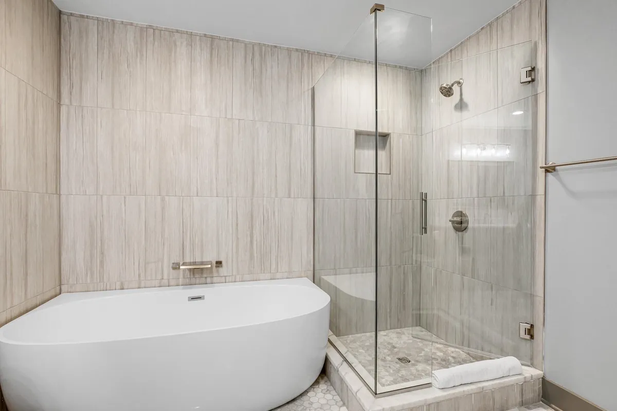 A modern bathroom with a freestanding bathtub, glass shower enclosure, and textured wall tiles. The setting is bright and spa-like, offering a tranquil and rejuvenating atmosphere for relaxation and self-care.
